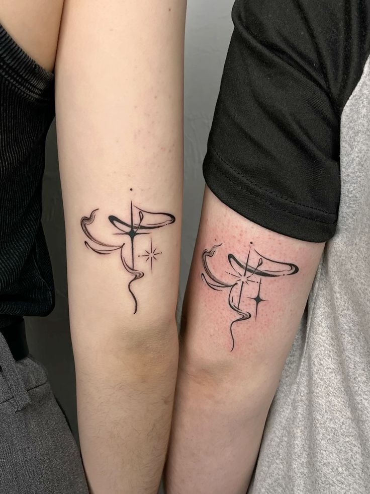 Minimalist matching tattoos on two arms, featuring abstract line designs and a small star symbol.